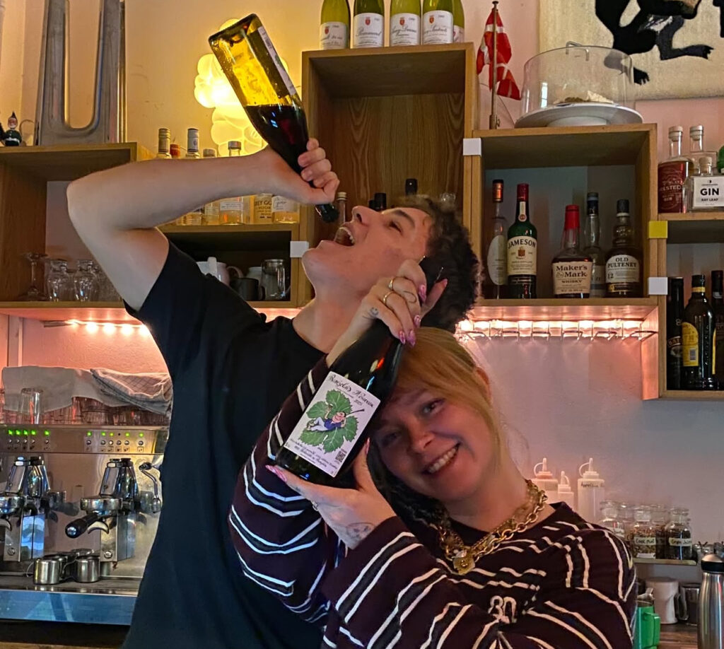 Ung mand lader som om han bæller rødvin ved siden af en ung kvinde, der smiler og holder en flaske vin.