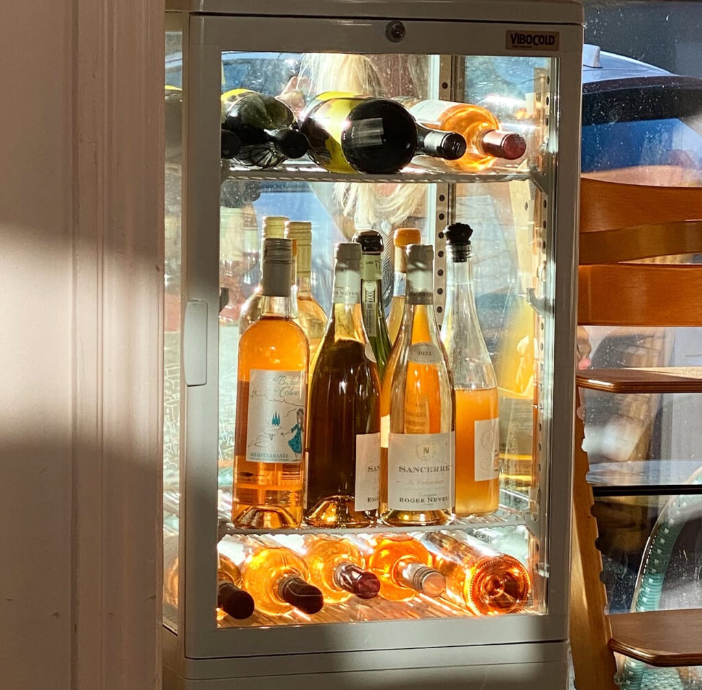”Mange orangevine og hvidvine står i en køleboks med sollys gennem bagsiden af glas”