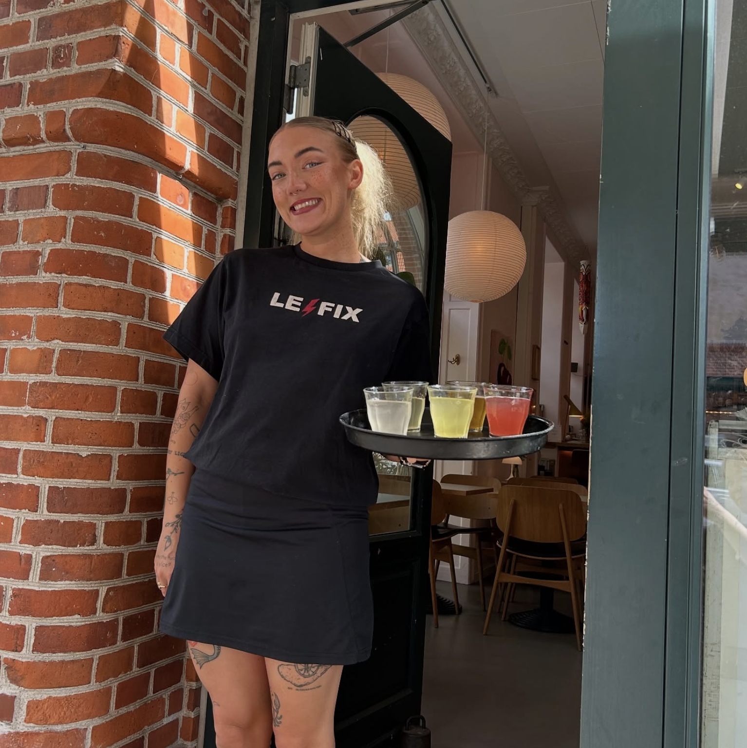 Sabina Larsen står med drinks på en bakke, mens hun smiler.