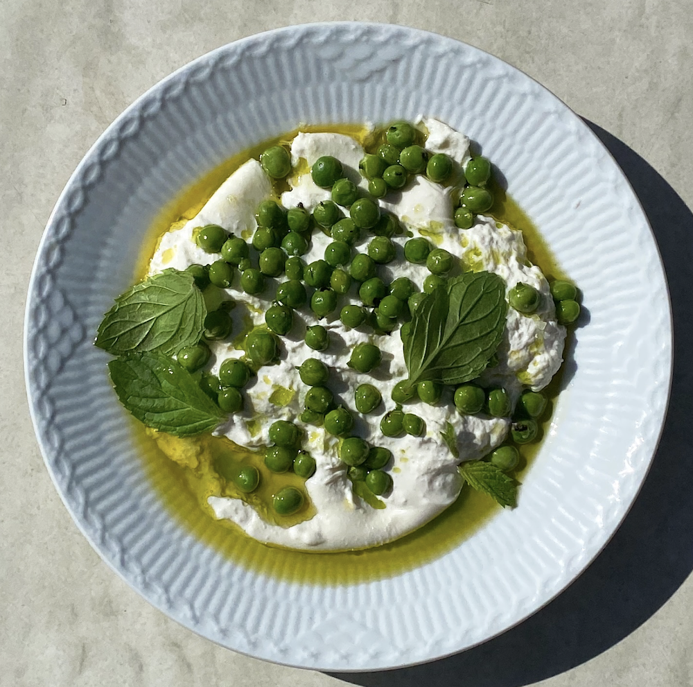 “En hvid tallerken med dansk øko burrata med grillede ærter og mynte”