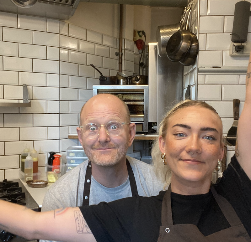 Tobias faber og Sabina Larsen står i køkkenet og smiler og stirrer til kameraet.